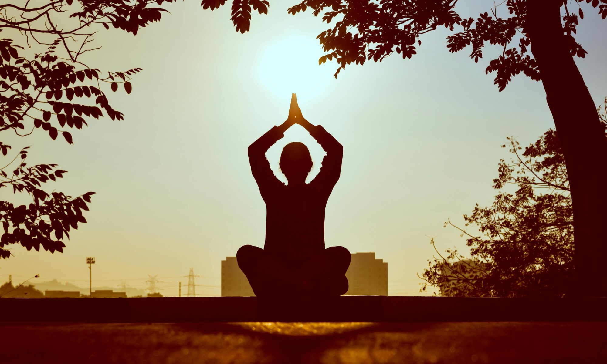 Im Gegenlicht der aufgehenden Sonne macht jemand eine Yogaübung. Dies Stimmung ist friedlich und warm.